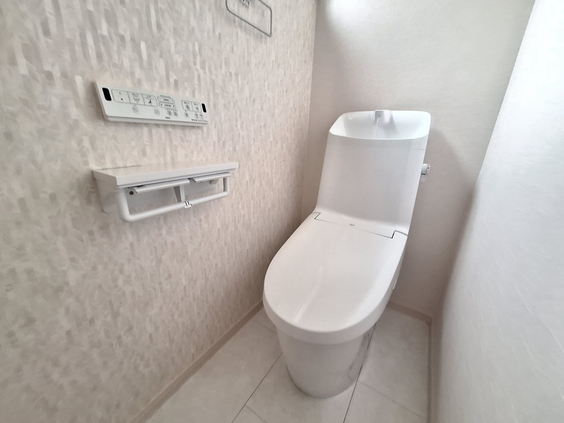 【設備画像：ベーシアシャワートイレ（LIXIL）】フチレス形状やお掃除リフトアップ機能などお手入れのしやすさが特徴。壁設置型のリモコンと２連紙巻き器が備え付けとなっている超節水タイプです。