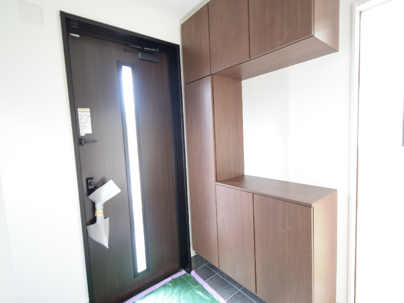 【２号棟：玄関】玄関には天井までの高さを活かした収納力あるシューズボックスを備え、白い壁にブラウンが映える落ち着いた空間になっています
