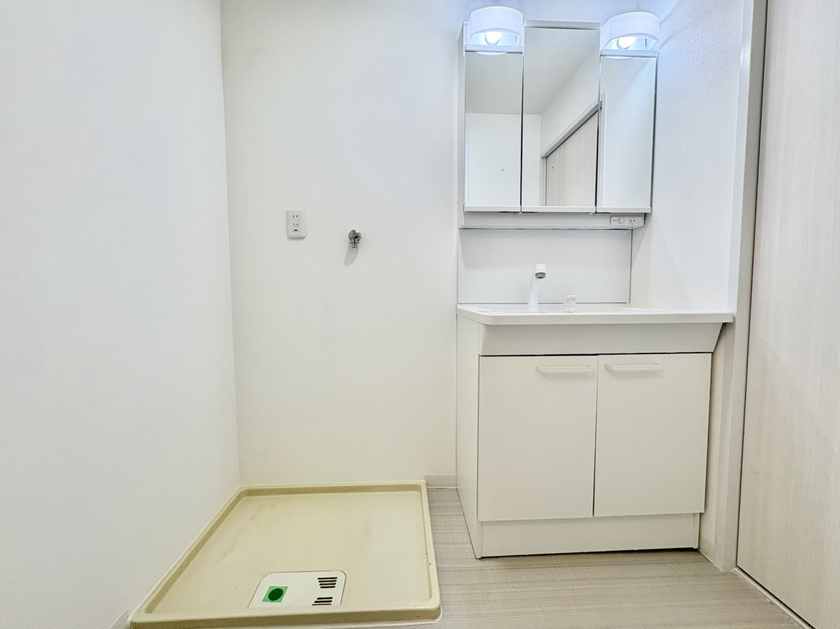 荒神山マンションの独立洗面台|身支度に便利な三面鏡付き洗面台。鏡裏や足元に豊富な収納を完備し小物をすっきり片付けられます。すぐ横に洗濯機置き場が並ぶスムーズな家事動線も魅力で、毎日の生活ワークを快適にサポートする洗面室です。