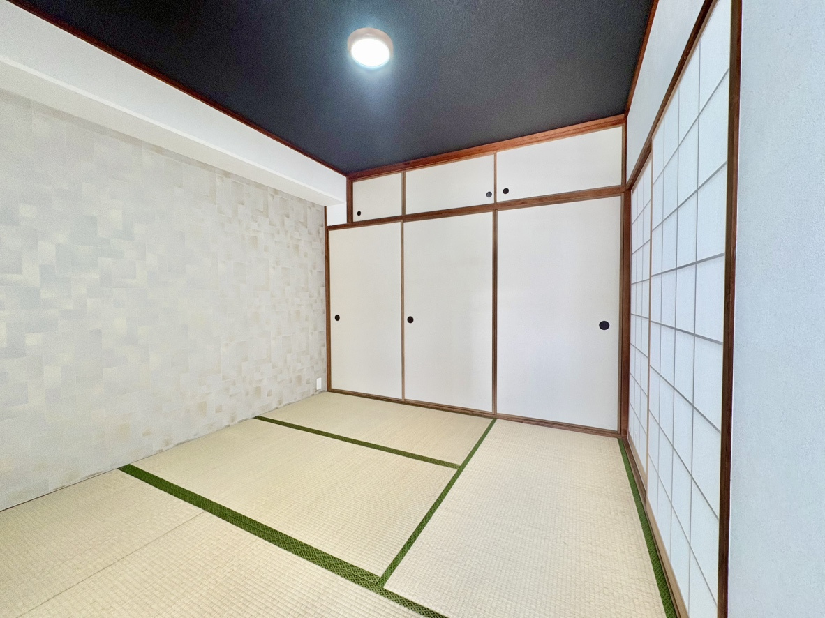 荒神山マンションの和室|黒天井とアクセントクロスが目を惹く和モダンな約4.5帖の和室。天袋付きの大容量押し入れを完備し、お布団や荷物をすっきり収納できます。畳の温かみと高いデザイン性を兼ね備えた、心地よい空間です。