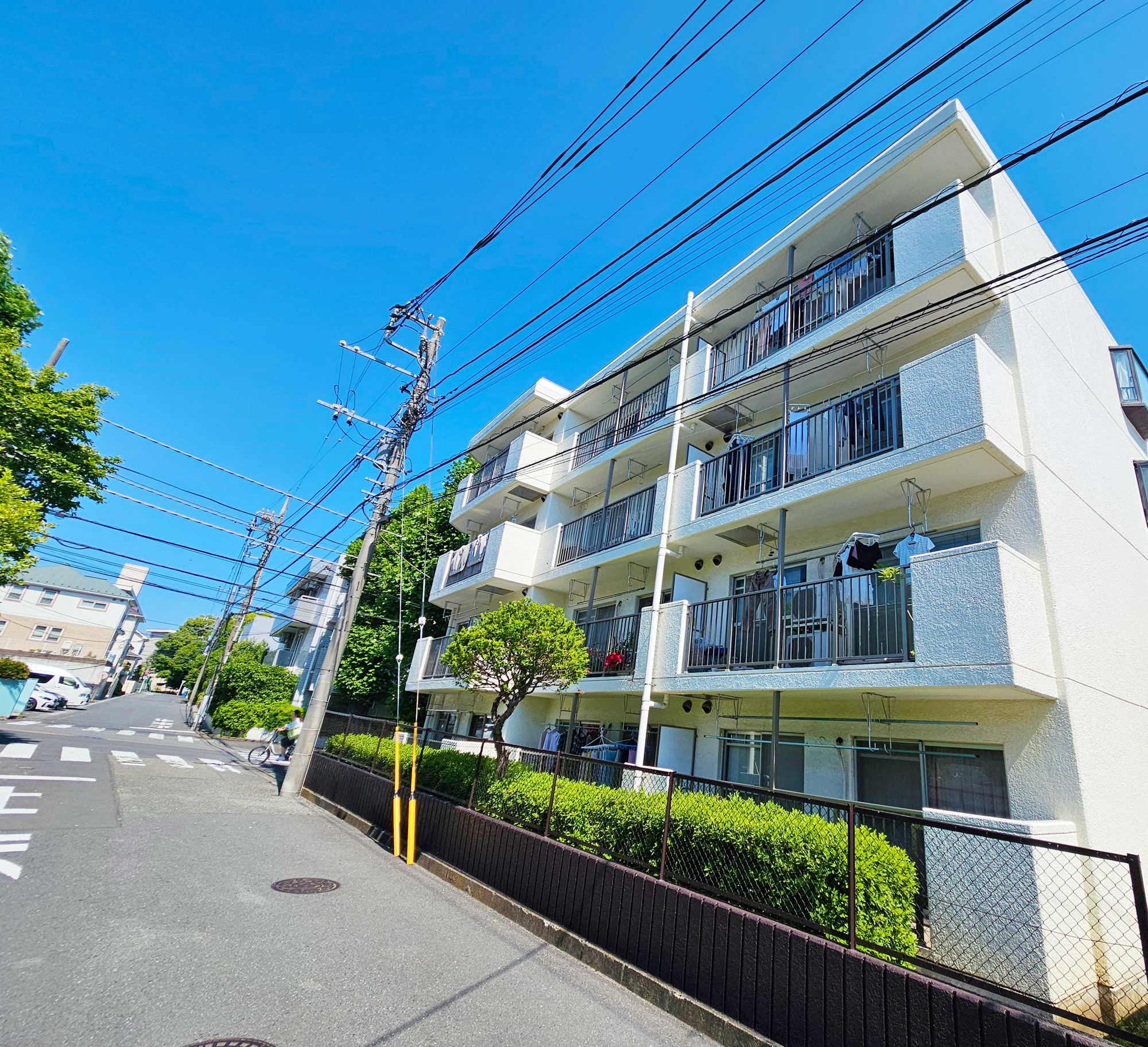 「鷺沼」駅徒歩20分◆2025年11月新規リノベ済◆鷺沼すみれが丘スカイマンションの外観|鷺沼駅徒歩20分！コンビニ・スーパー徒歩圏内に複数あり◎青空に映える爽やかな白い外観。周辺は緑豊かで子育てファミリーにもぴったりの穏やかな住環境です。前面道路も広くすっきりとしています。