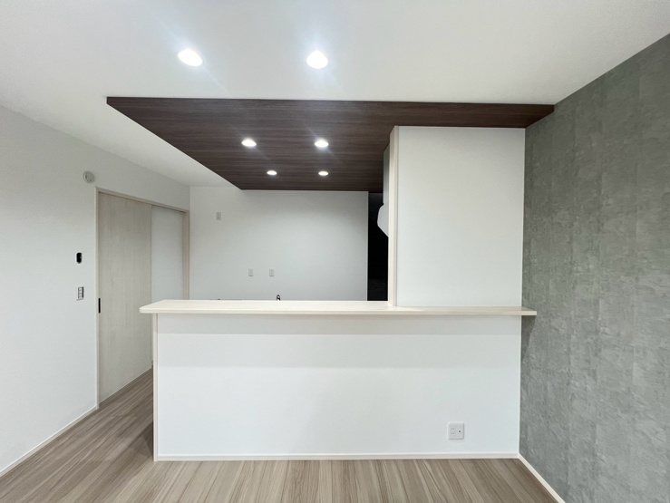 【坂戸市片柳2号棟 キッチン折下げ天井】空間を緩やかに仕切り、キッチンをおしゃれで落ち着いた雰囲気に。木目調や照明演出で洗練された高級感あるリビングを叶えます。