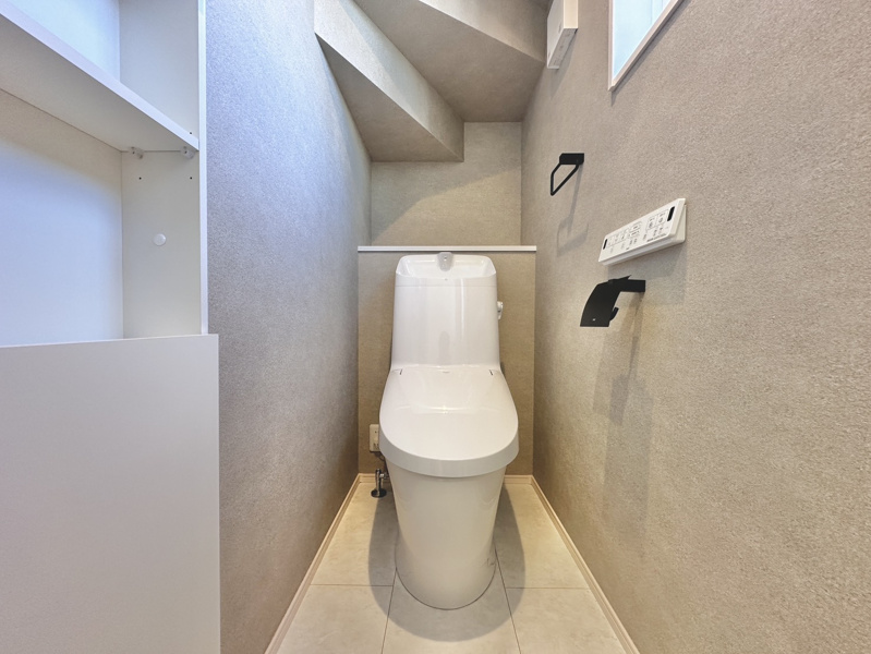 清潔感あふれる温水洗浄便座付きのトイレスペース！階段下の空間を賢く活用し、予備のトイレットペーパーや清掃用品をサッと置ける棚を設置♪お掃除もしやすいスリムなデザインで快適に利用できますね！